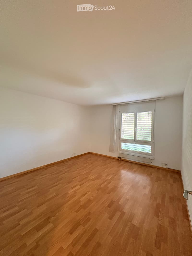 Empty room with wooden flooring, white walls, and a window with blinds.