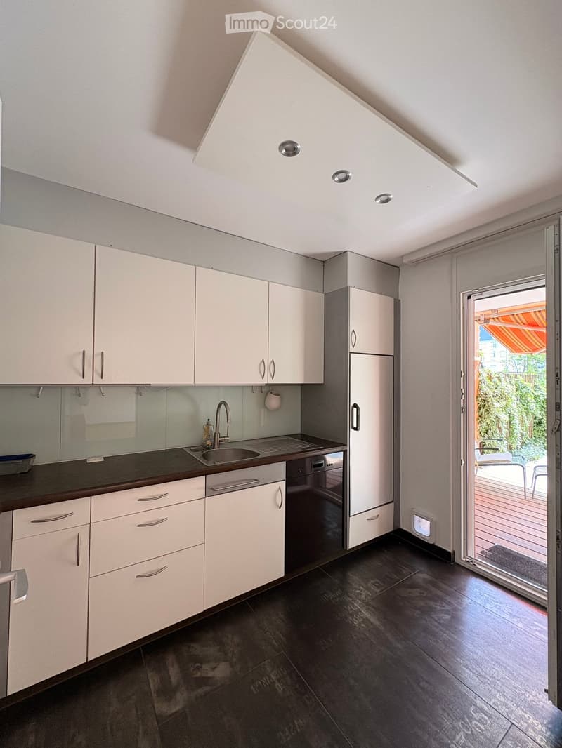 Modern kitchen with white cabinets, stainless steel sink, dishwasher, and refrigerator. Features a sliding glass door leading to a balcony or terrace.