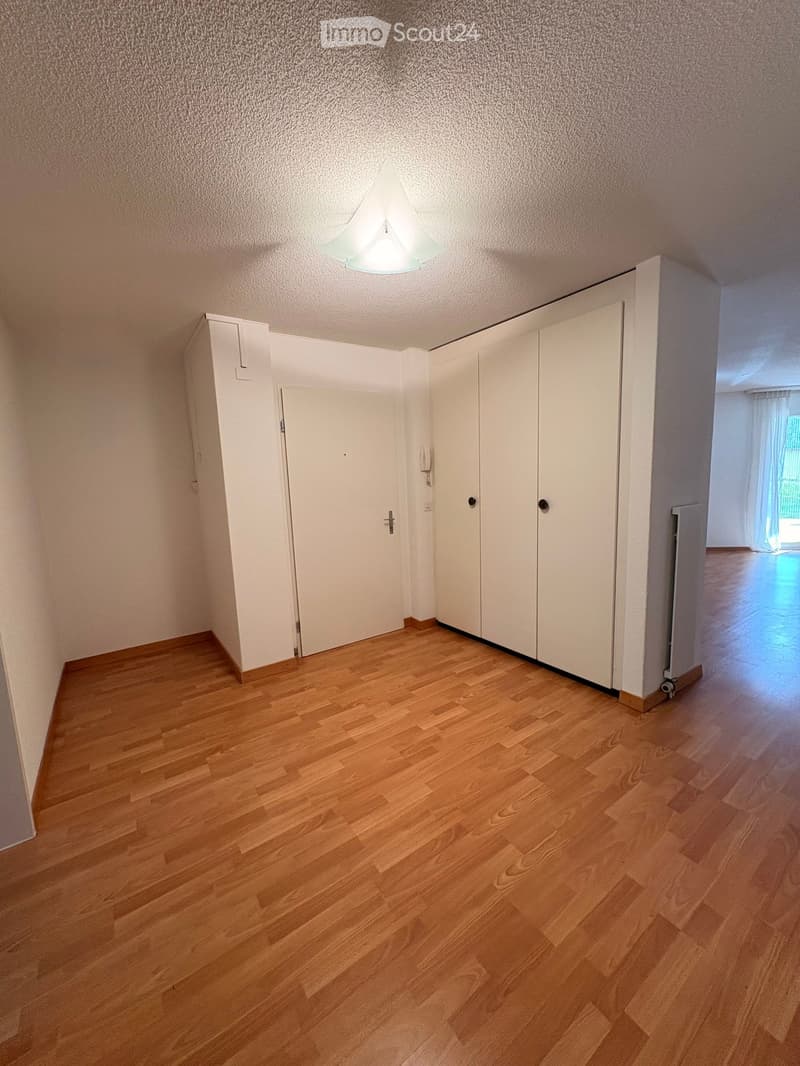 Empty hallway with wooden flooring, white walls, and a ceiling light fixture. There are white doors and a radiator visible.