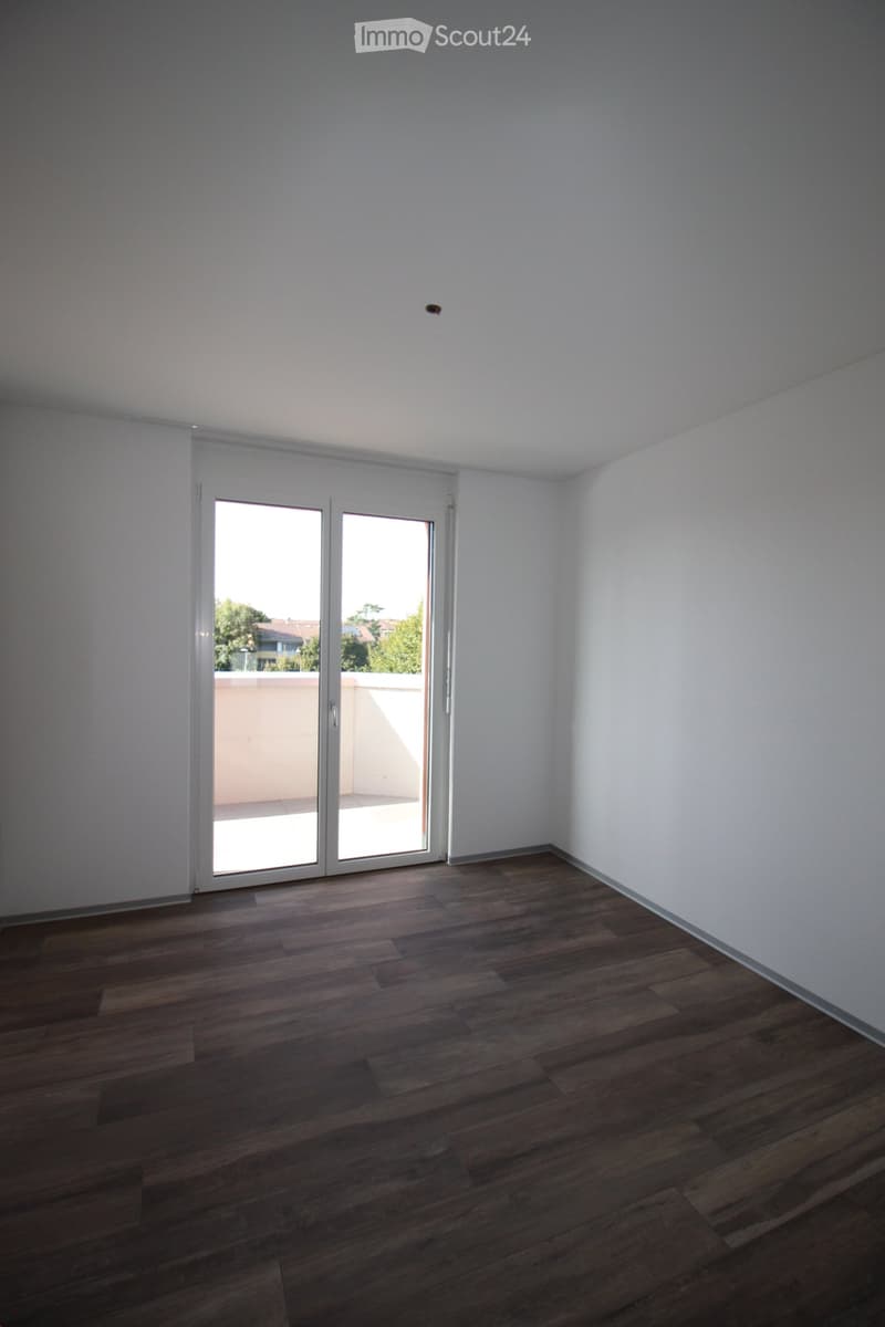 Empty room with wooden flooring, white walls, and a large sliding glass door leading to a balcony.