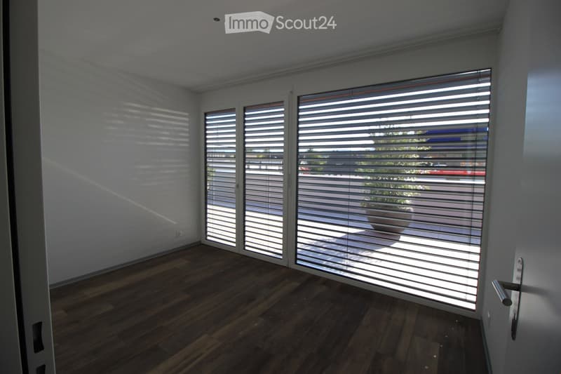 Empty room with wooden flooring, white walls, and large windows with blinds. No furniture or equipment visible.