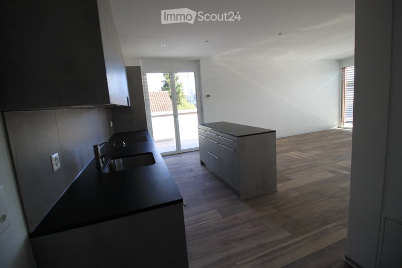 Modern kitchen with dark countertops, wooden flooring, and built-in cabinets. Features a sink with a modern faucet and a central island with drawers.