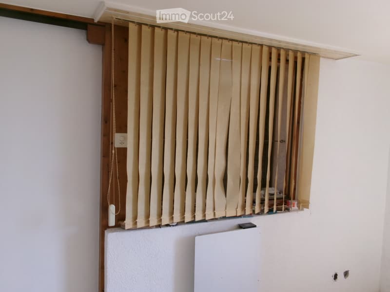 Empty room with white walls, a window covered by vertical blinds, and a radiator below the window.