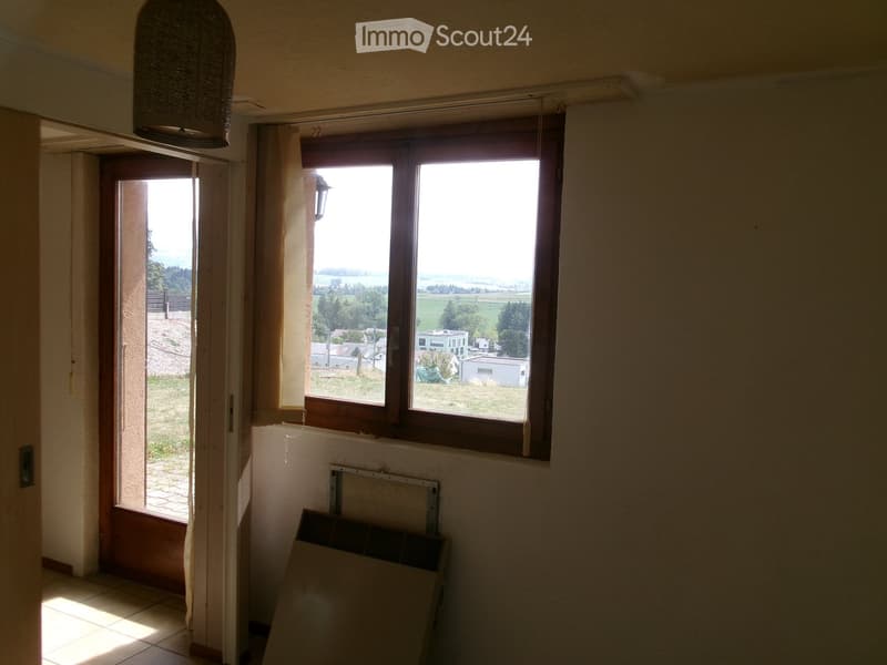 Empty hallway with tiled floor, large window showing a view of a rural landscape, and a partially open door leading outside.