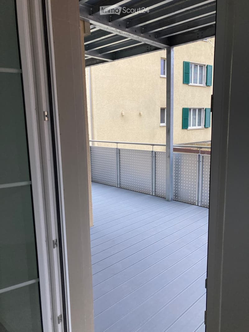 Balcony with wooden decking, metal railing, and view of neighboring building with green shutters.