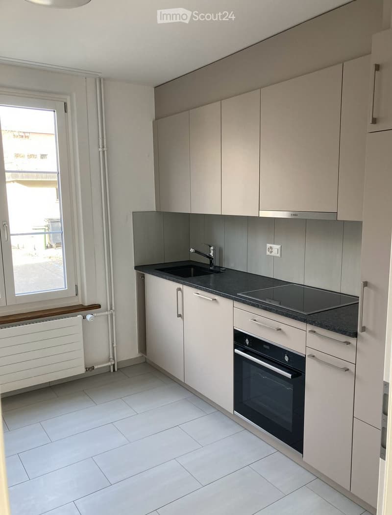 Modern kitchen with white cabinets, black countertops, a sink, a stove, and an oven. The space is well-lit with a window providing natural light.