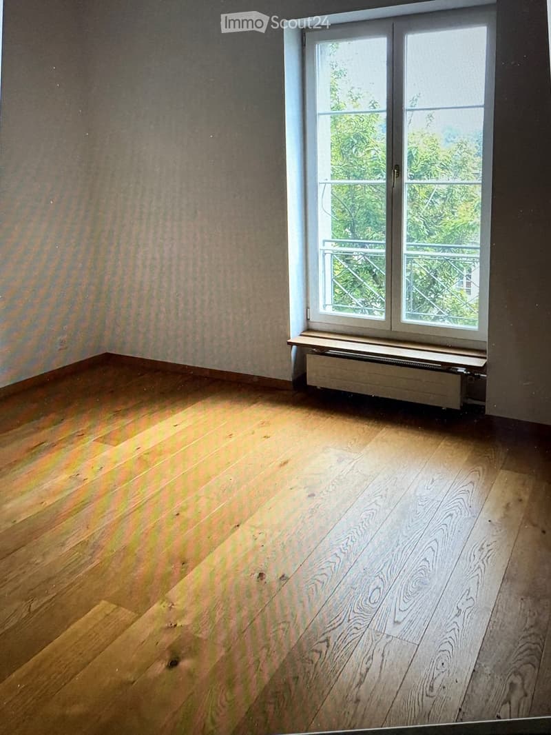 Empty room with wooden flooring and a window with a radiator below it. The walls are painted in a neutral tone.