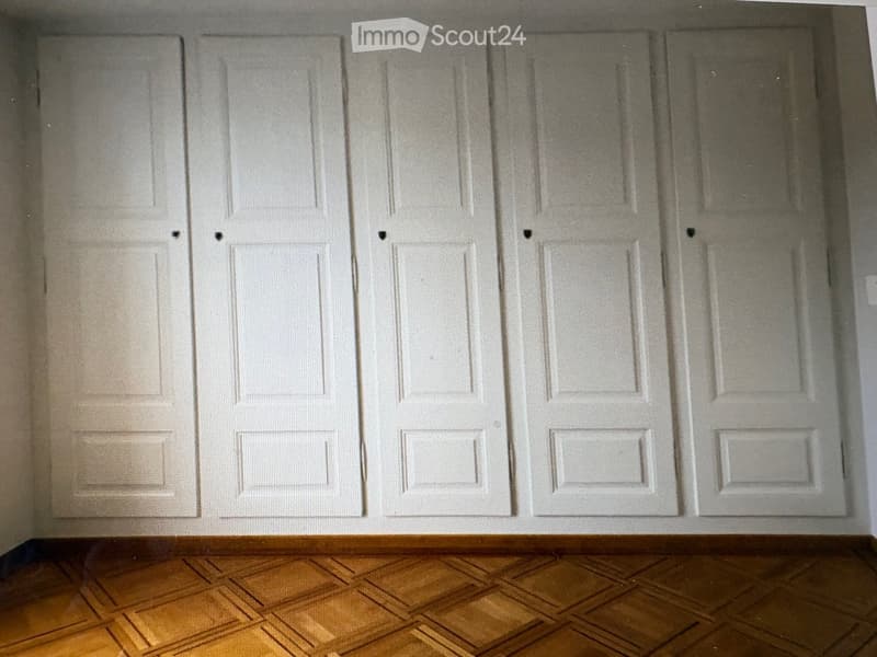 Empty room with wooden floor and multiple white doors.