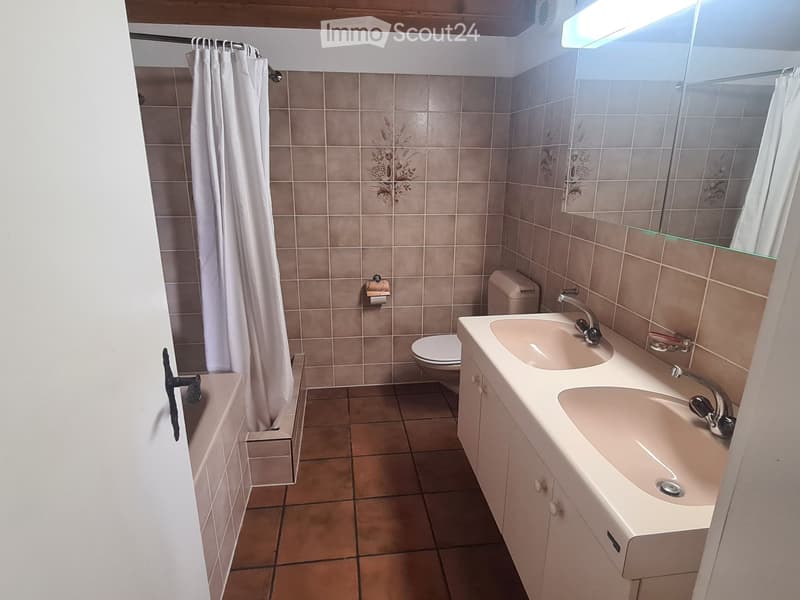 Bathroom with beige tiles, double sink, toilet, bathtub, and a large mirror above the sink.