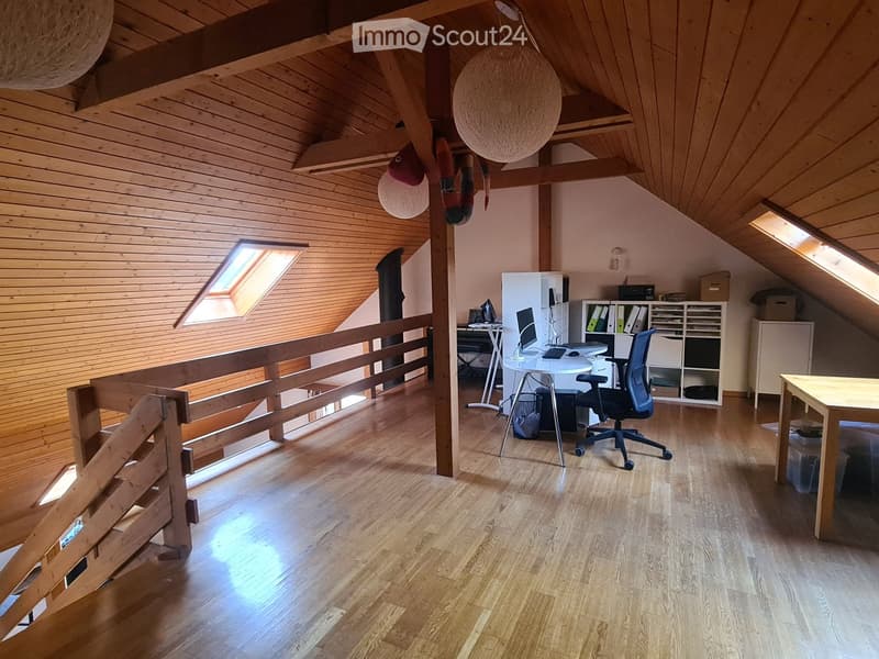 Bright, wooden-floored attic room with exposed wooden beams, skylights, a desk with a laptop, a chair, and a bookshelf.