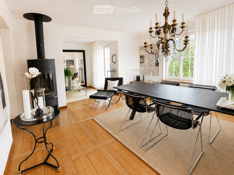 Modern dining area with a black dining table, black chairs, a chandelier, a fireplace, and a small round table with a vase of white flowers.