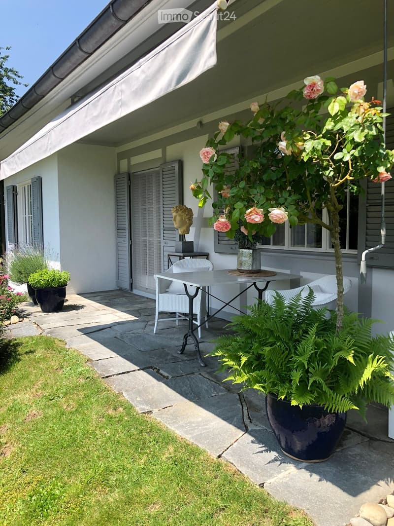 Outdoor patio area with a table, chairs, potted plants, and a sculpture near the house entrance.
