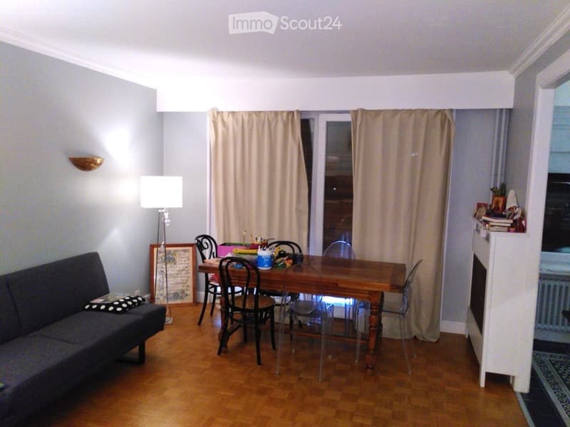 A modern living and dining area with a grey sofa, wooden dining table, chairs, floor lamp, and a picture frame on the wall.