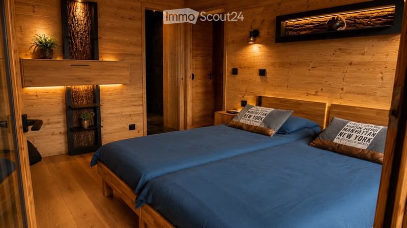 Cozy wooden bedroom with two single beds, nightstand, potted plants, and built-in shelving with decorative items.