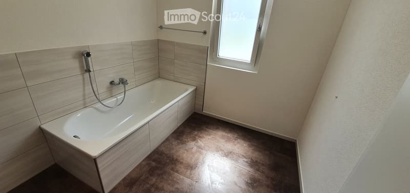 Modern bathroom with a bathtub, tiled walls, a window, and a towel rack.