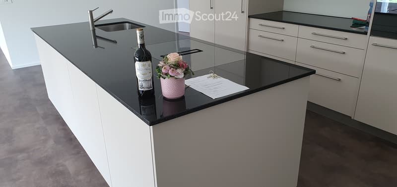 Modern kitchen with white cabinets, black countertops, a central island, a bottle, a flower vase, and a faucet.