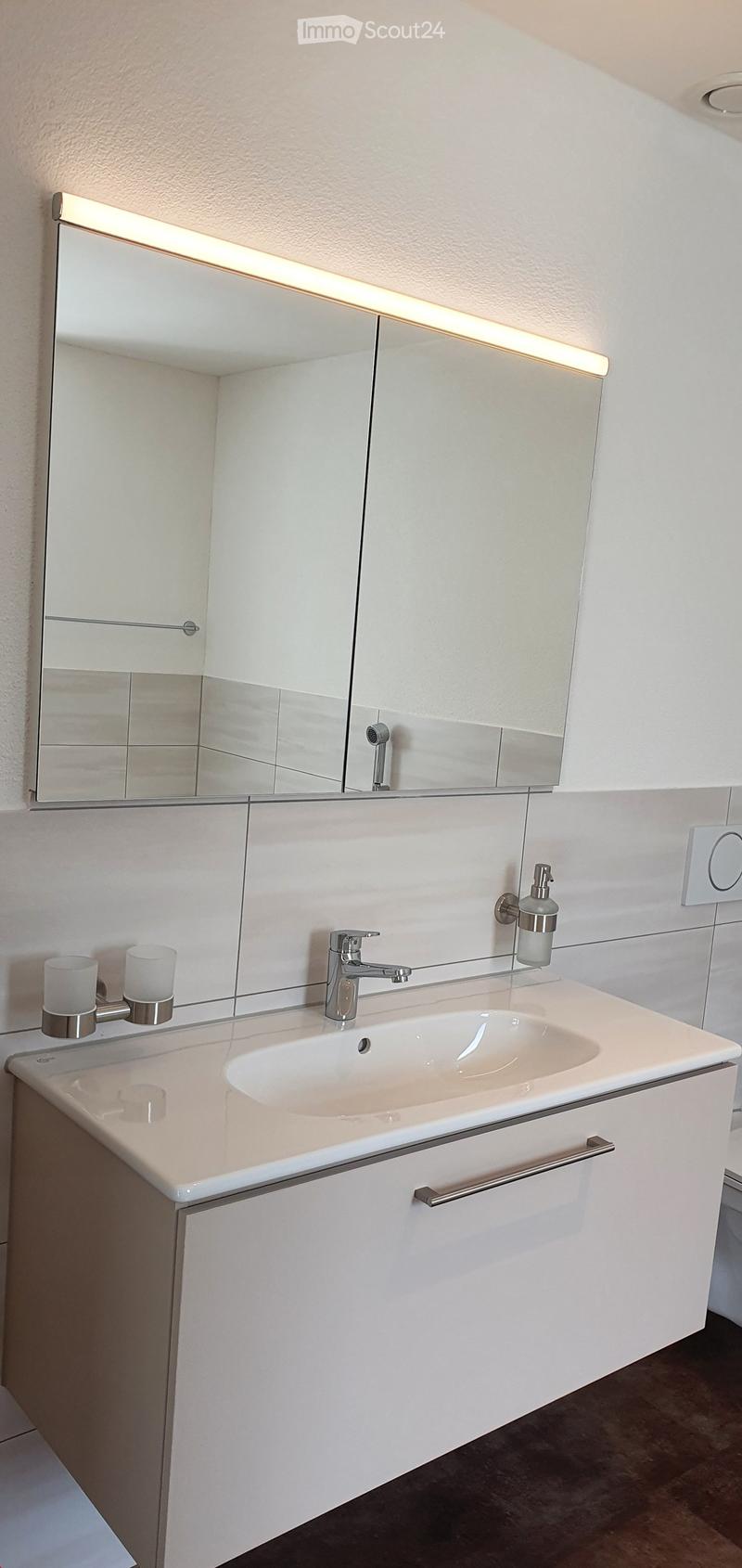 Modern bathroom with a white sink, chrome faucet, large mirror with integrated lighting, and two decorative candles on the countertop.