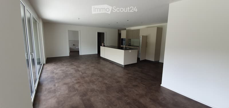 Modern kitchen with white cabinets, a central island, and dark flooring. The space is open and well-lit with large windows and doors leading to another room.