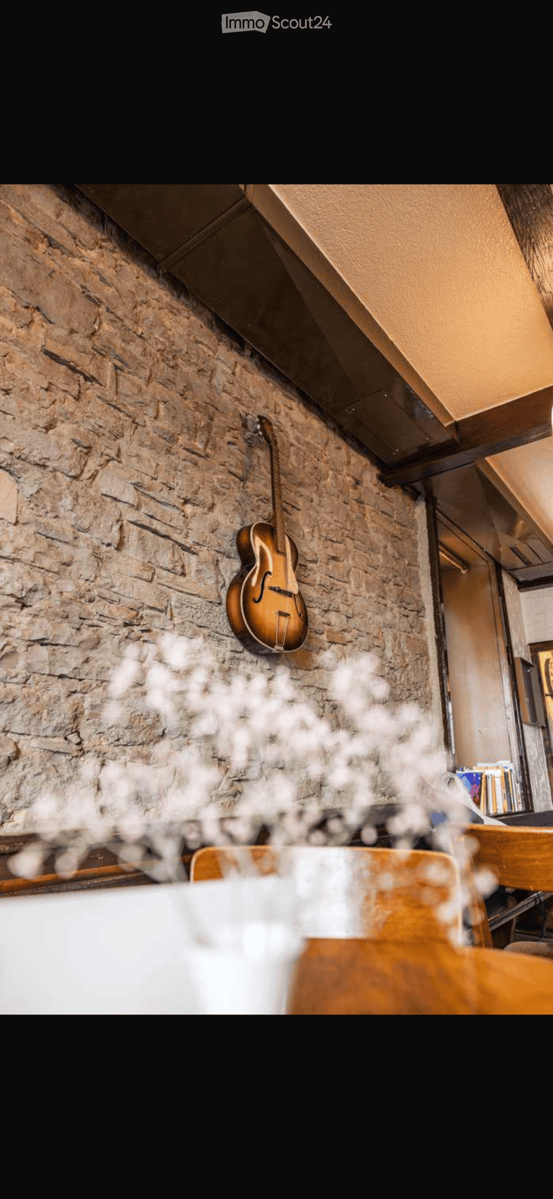 A cozy room with exposed brick walls, a wooden guitar hanging on the wall, a wooden table, and a chair.