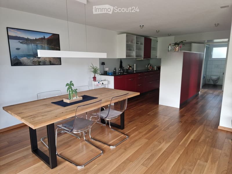 Modern kitchen with wooden dining table, chairs, cabinets, sink, and a framed picture on the wall.