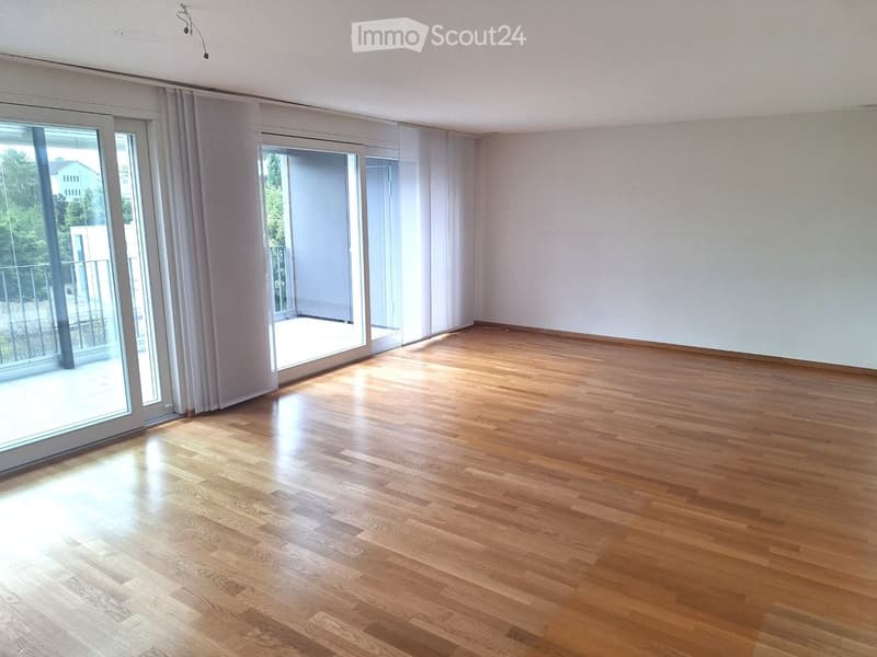 Empty room with wooden flooring, large sliding glass doors leading to a balcony, and white walls.