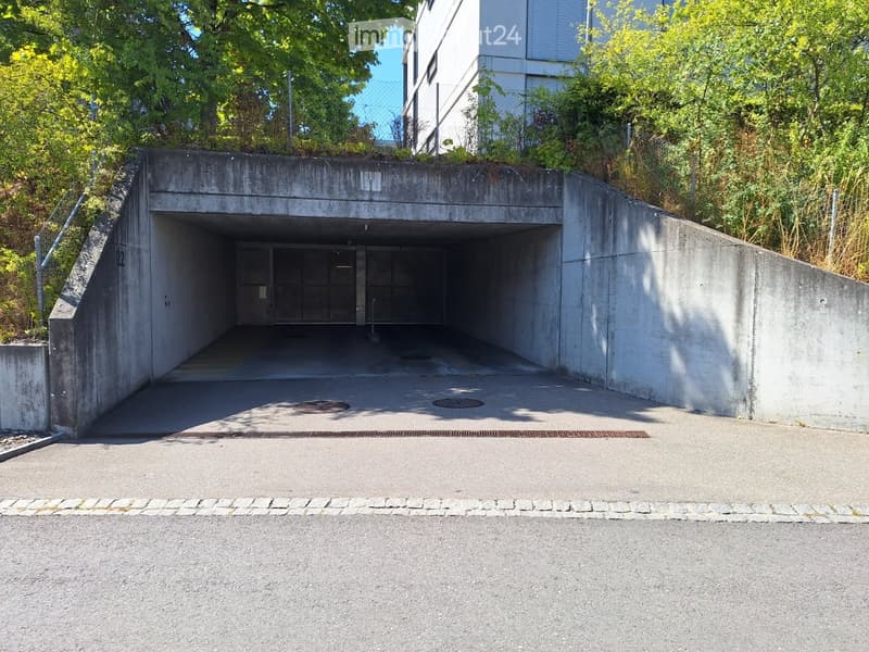 Underground parking entrance with concrete walls and a raised ground floor leading up to a modern building.