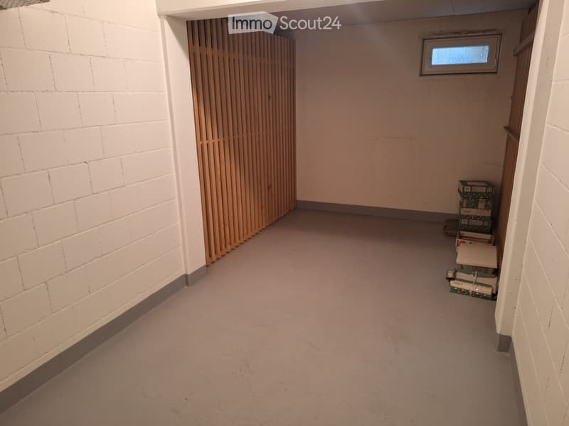 Empty hallway with white brick walls, a wooden panel door, and a small window at the far end. Some stacked boxes are visible on the right side.