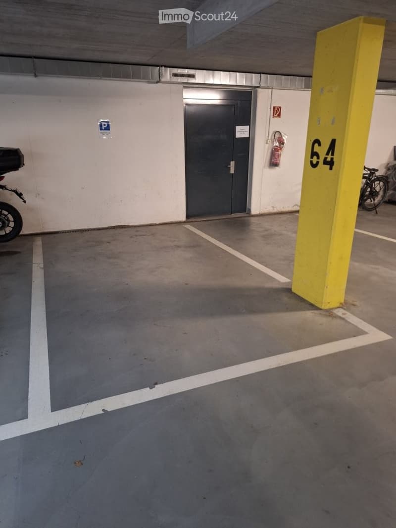 Underground parking area with marked parking spaces, a yellow pillar marked '64', a closed metal door, and a fire extinguisher mounted on the wall.