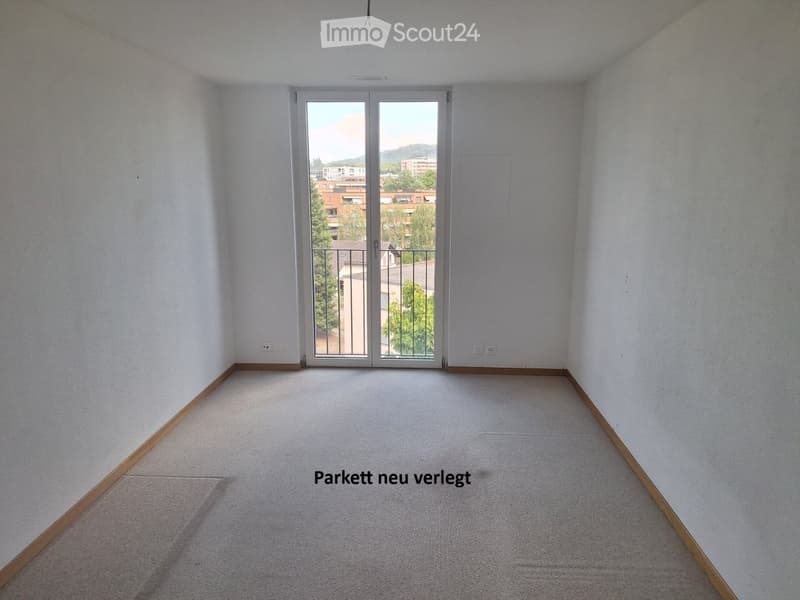 Empty room with light-colored walls, carpeted floor, and large sliding glass door leading to a balcony.