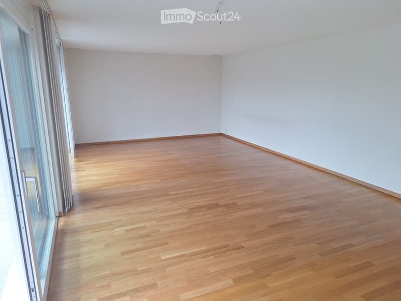 Empty room with wooden flooring and white walls, featuring large glass sliding doors with curtains.