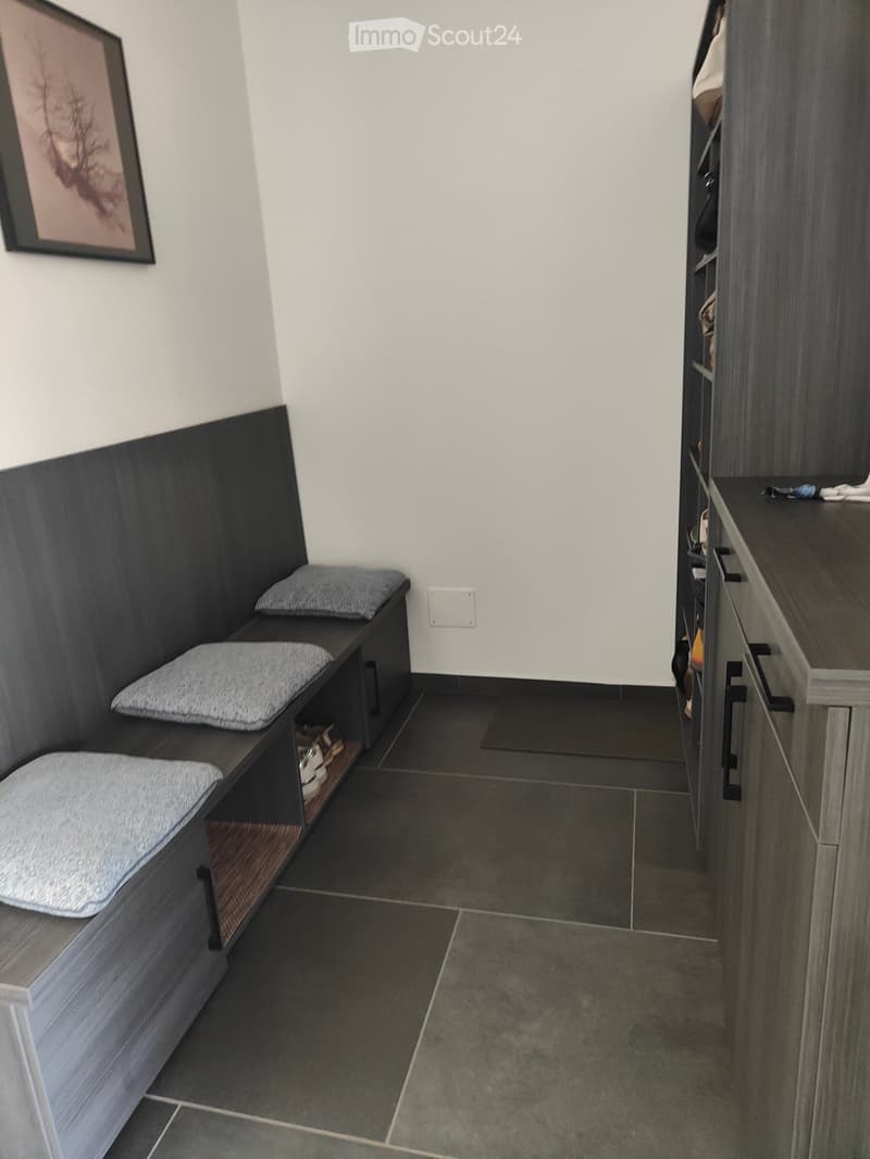 Modern hallway with dark tiled floor, built-in bench with cushions, shoe storage, and a small cabinet with drawers.