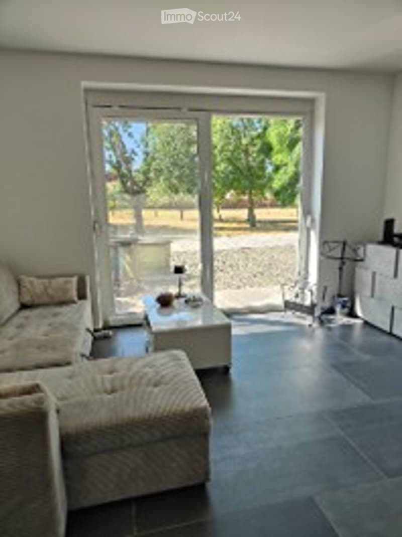 Bright living room with large sliding glass doors leading to a balcony, a comfortable sofa, coffee table, side table, and a storage unit.