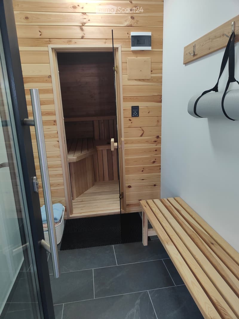 Bathroom with wooden sauna bench, control panel, towel rack, and a towel visible near the entrance.