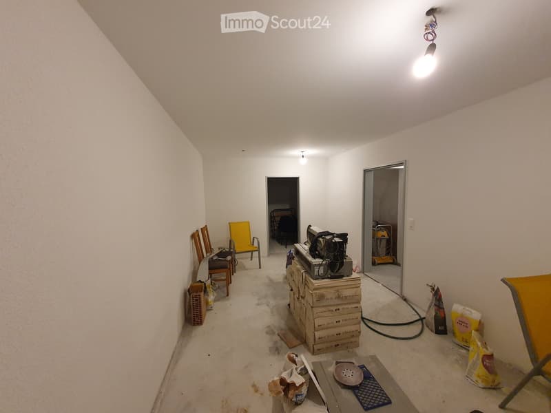 A partially furnished room with a chair, table, and screen, along with various construction materials and tools.
