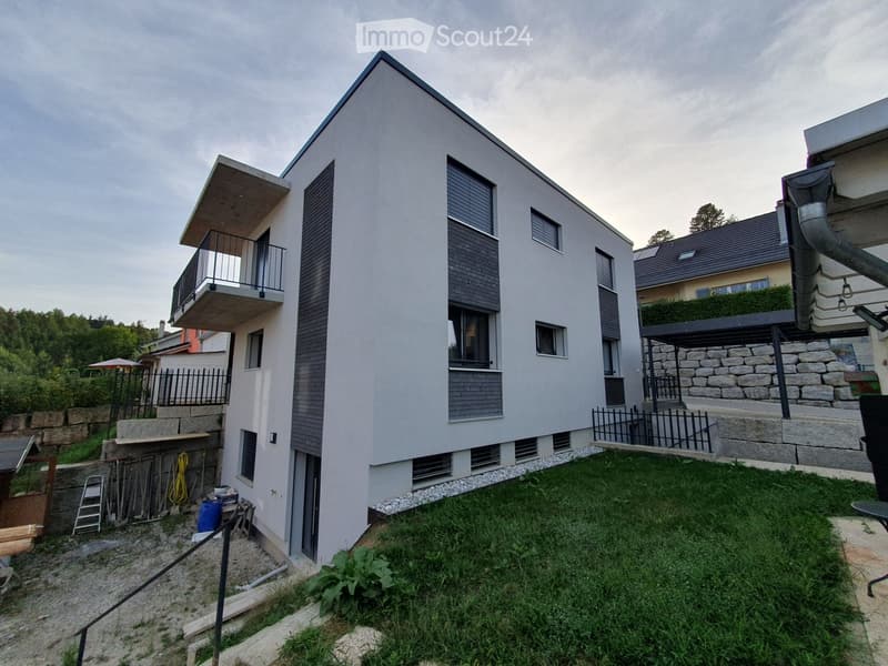 Modern two-story house with a raised ground floor, balcony, and surrounding greenery.