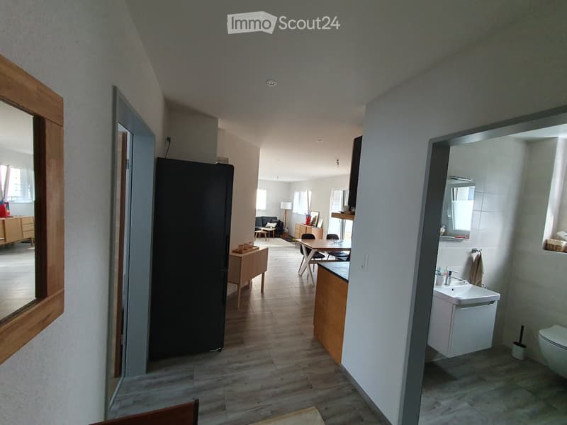 Hallway with wooden flooring, leading to a kitchen area with a dining table and chairs, and a bathroom with a sink and toilet.