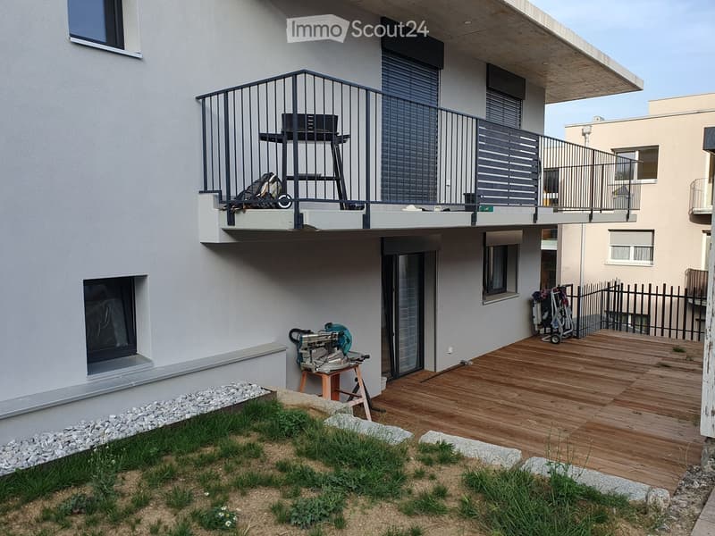 Balcony with metal railing, wooden deck, small garden area with rocks and plants, and a workbench with tools.