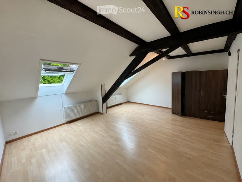 Empty attic room with wooden flooring, white walls, exposed wooden beams, built-in wardrobes, and skylight windows.