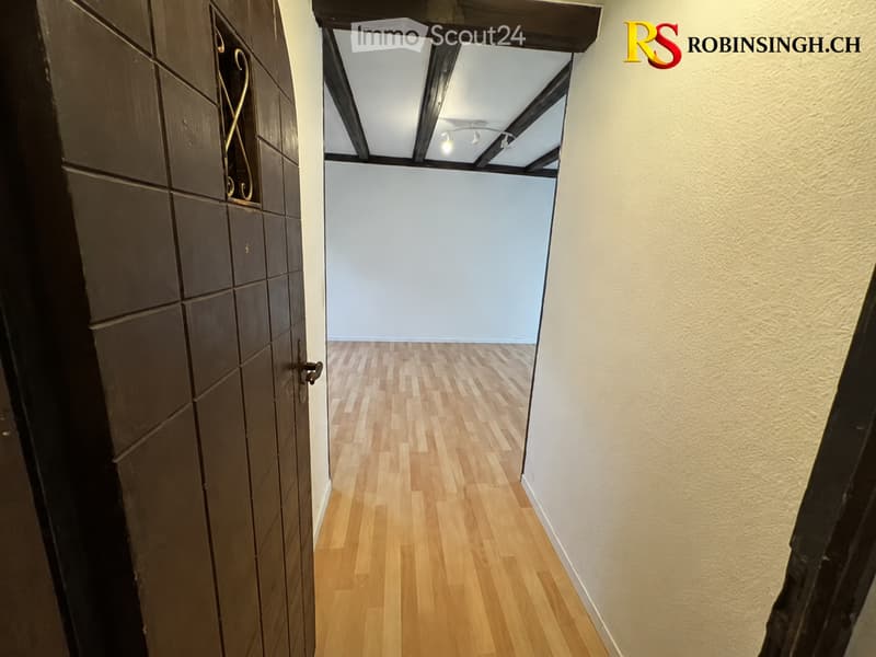 Empty hallway with wooden flooring, light blue walls, and a ceiling with exposed beams and lighting fixtures.