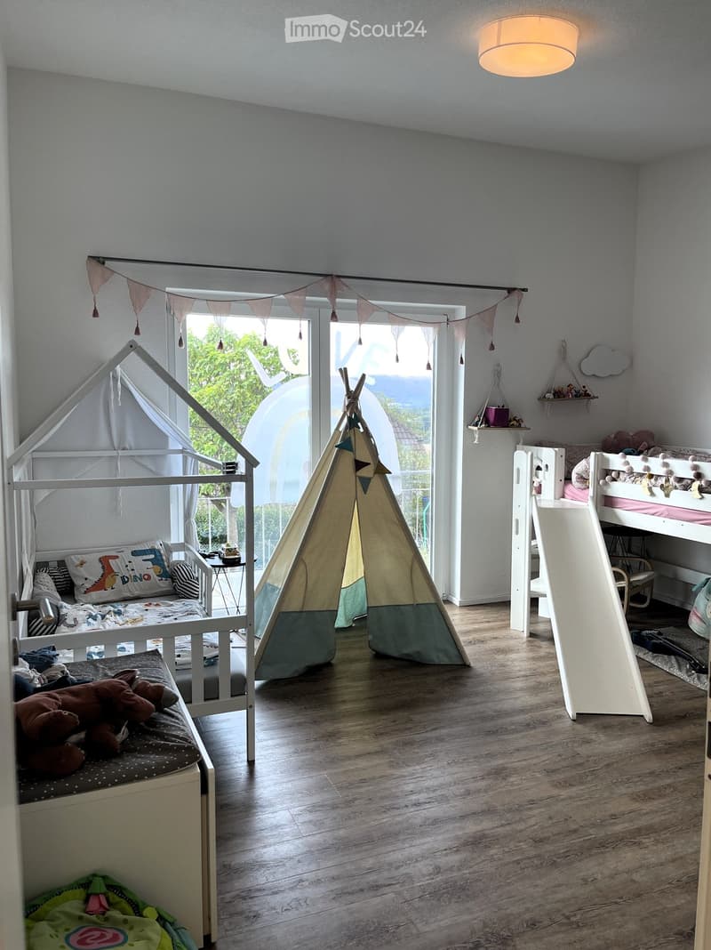 A well-lit children's bedroom with a bunk bed, a toy tent, a small bed, and various toys and decorations.