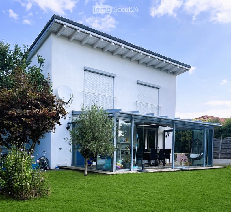 Modern single-story house with white exterior, large glass patio, outdoor dining area, and well-maintained lawn.