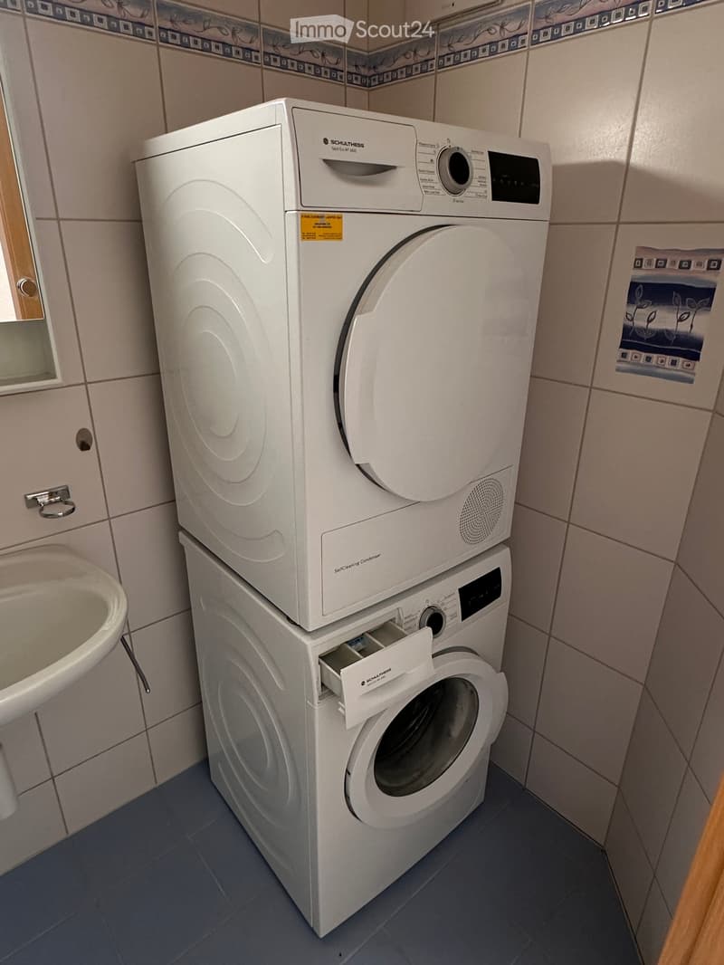 Bathroom with a white washing machine and dishwasher stacked, a sink, and tiled walls.