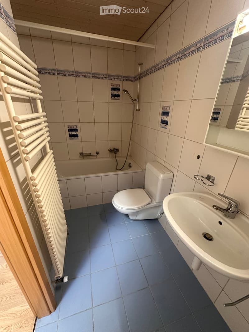 Modern bathroom with blue tiled floor, white tiled walls, a bathtub, toilet, sink, and a white radiator on the left side.