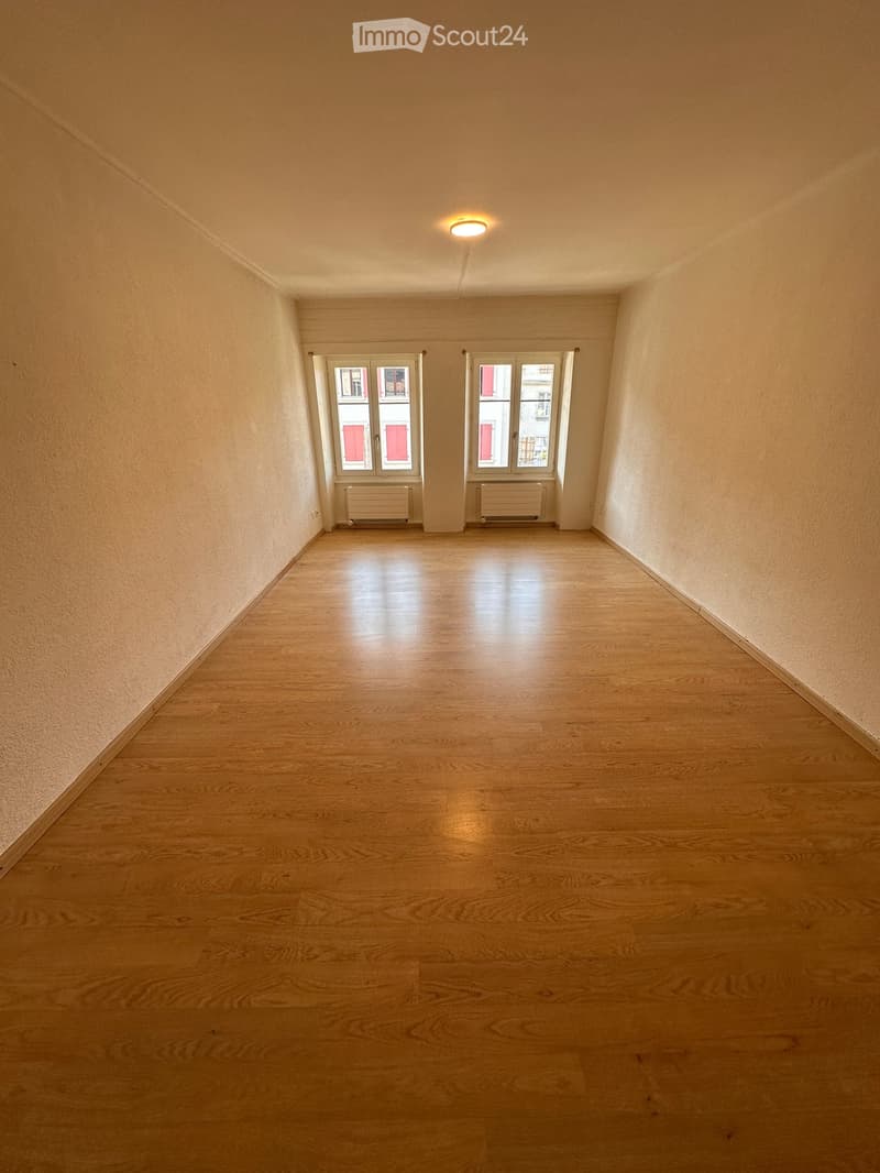 Empty room with wooden flooring, two windows, and a ceiling light fixture.