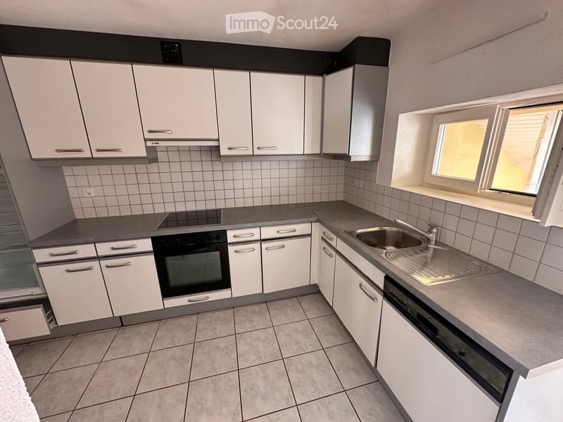 Modern kitchen with white cabinets, tiled walls, and grey countertops. Features a sink, oven, and dishwasher.