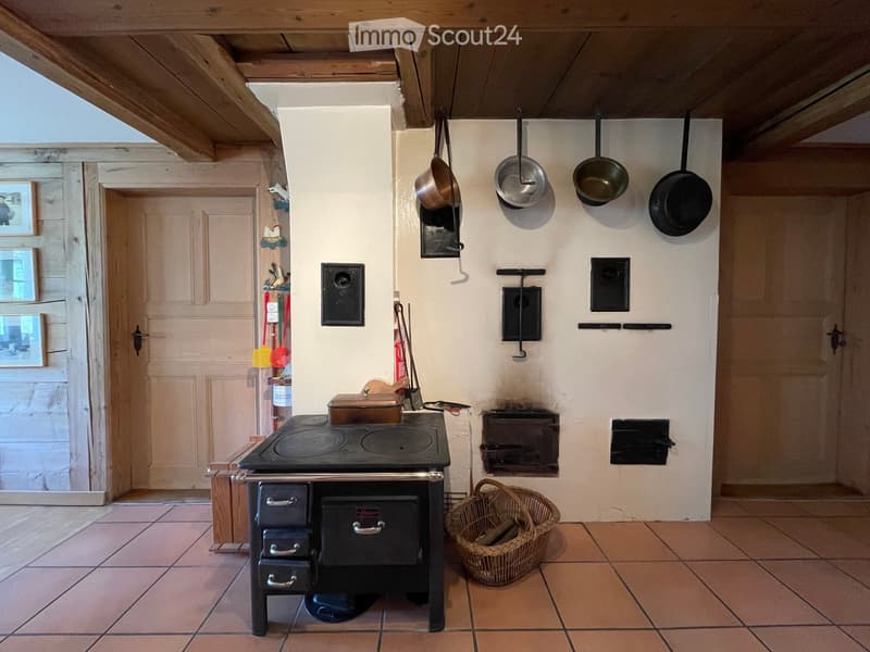 Traditional kitchen with a black cast-iron stove, hanging pots, a woven basket, and a wooden door leading to another room.