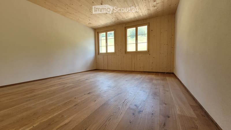 Empty room with wooden flooring, white walls, and two windows with wooden frames. The ceiling is also wooden, and the walls are painted in a light color.