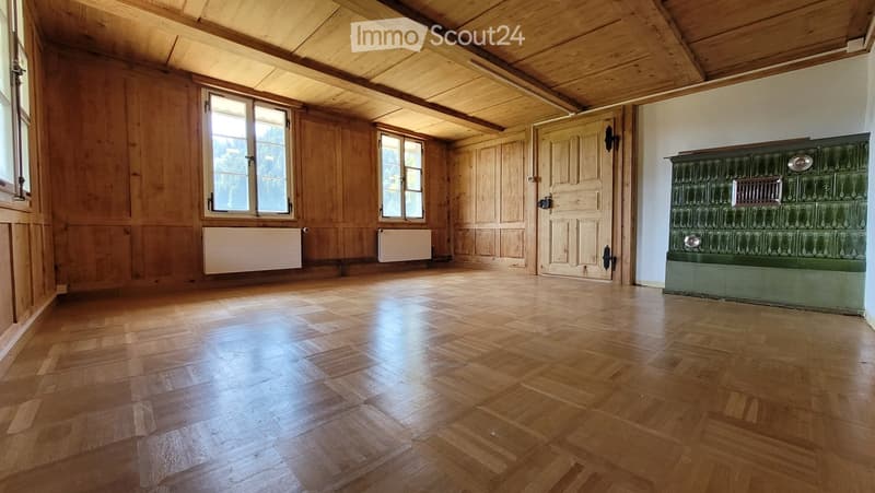 Empty room with wooden walls, wooden floor, large windows, and a green tiled stove.