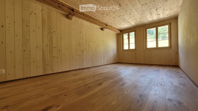 Empty room with wooden walls and floor, two windows, and exposed wooden beams on the ceiling.