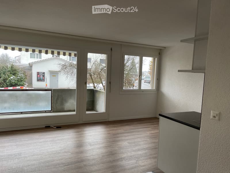 Empty room with wooden flooring, large windows, and a balcony area with a view of the street.